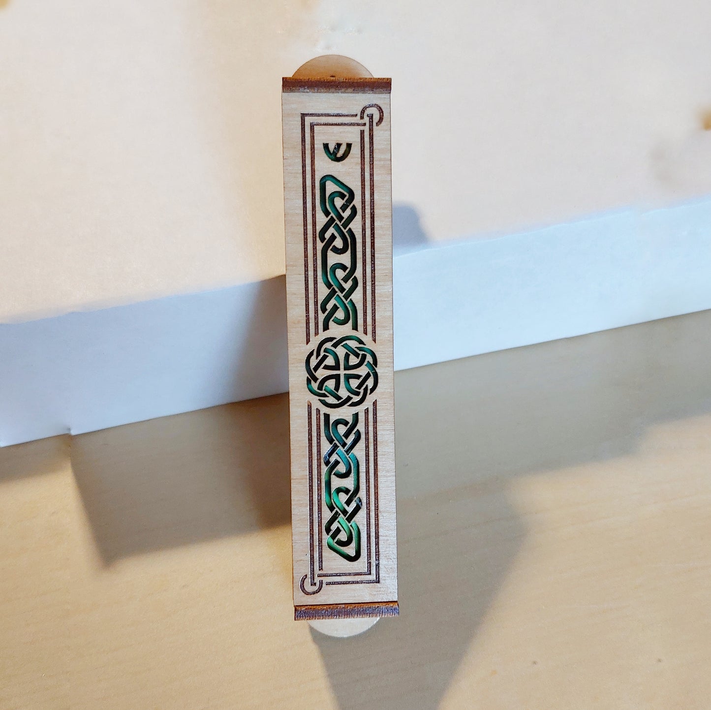 Wooden mezuzah case with cutouts of a celtic knot pattern with green background.