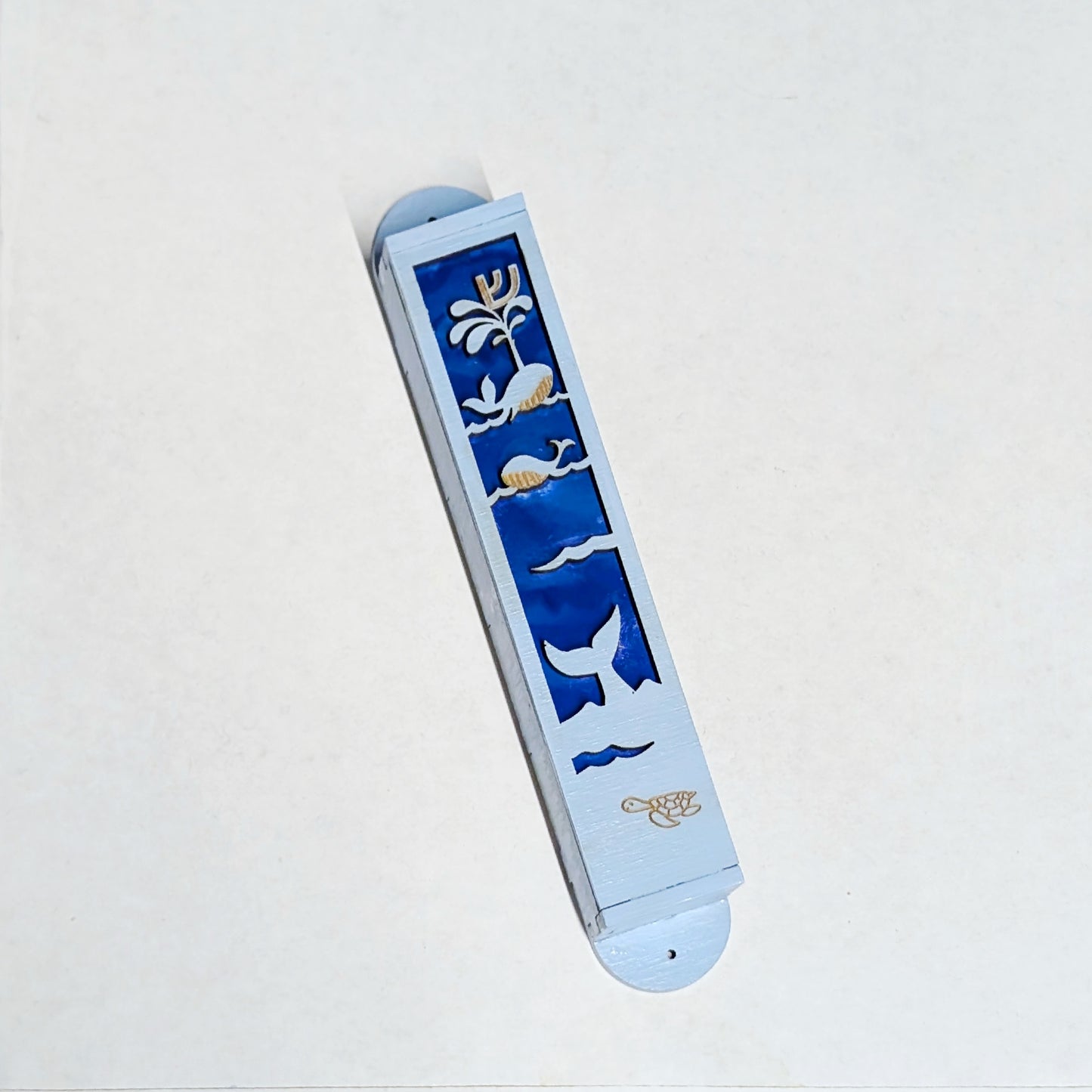 Light bue painted Mezuzah case with cut outs of whales over a dark blue background.