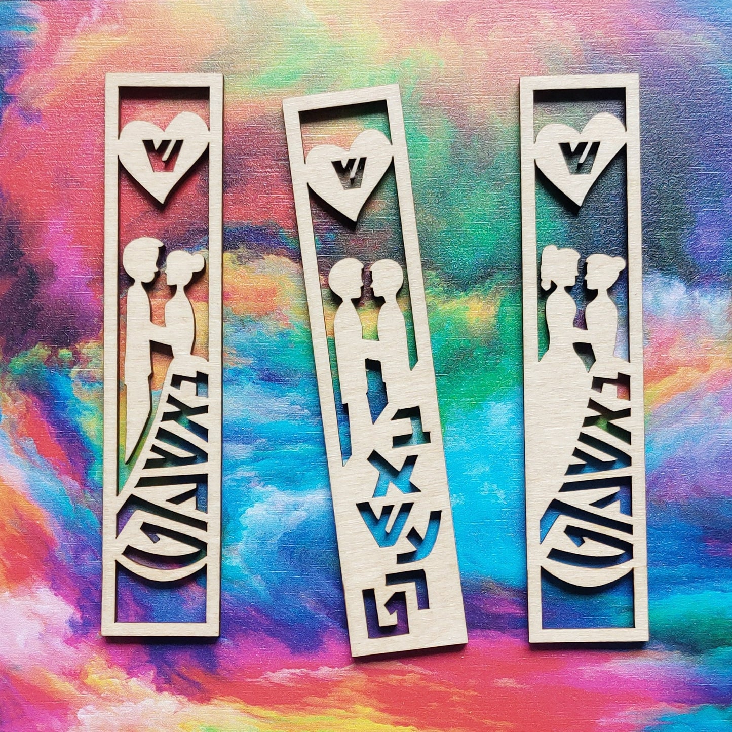 Three front pieces from mezuzah cases decorated with couples, the word "Bashert" in Yiddish, a heart with a shin, and rainbow swirl behind them. The first one has a person wearing a suit and a person wearing a dress, the second two people wearing suits, and the third has two people wearing dresses.