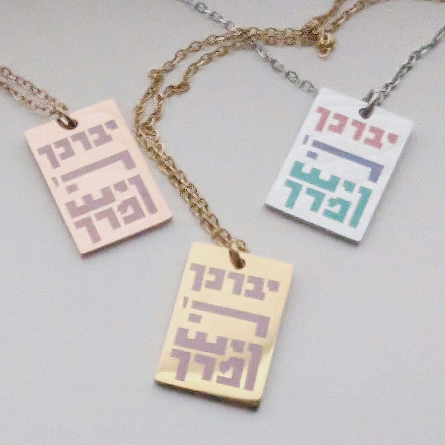 3 rectangle necklace pendants with Hebrew letters spelling out the priestly blessing. One silver, one rose gold, and one gold.
יברך ה' וישמרך
"Yivarechecha Hashem ViYishmarecha"