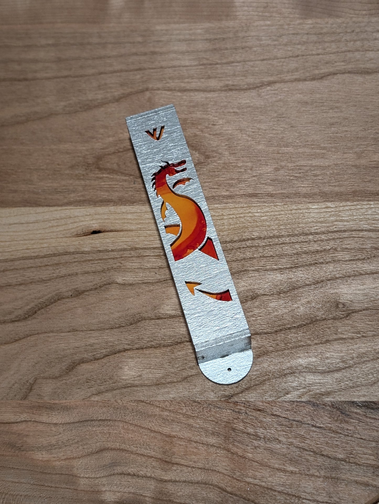 Silver painted mezuzah case with the cutout of a dragon and orange painted background showing through.