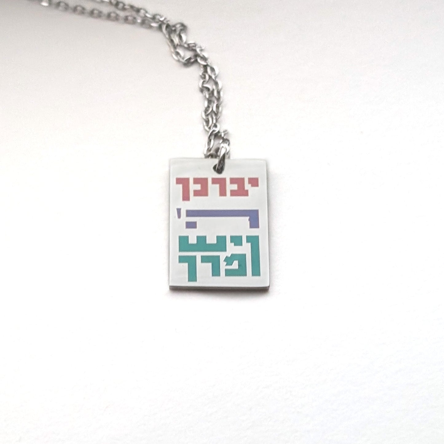Gold colored rectangle pendant with mullticolor hebrew letters spelling out the children's blessing.
יברך ה' וישמרך
"Yivarechecha Hashem ViYishmarecha"