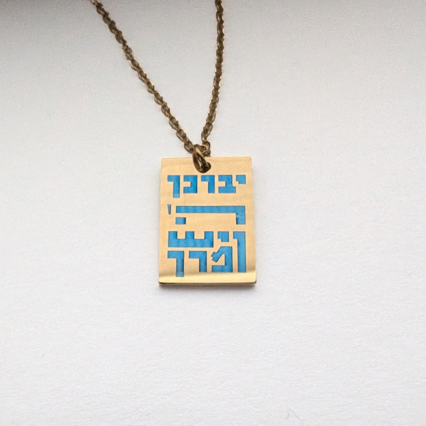 Gold colored rectangle pendant with blue hebrew letters spelling out the children's blessing.
יברך ה' וישמרך
"Yivarechecha Hashem ViYishmarecha"