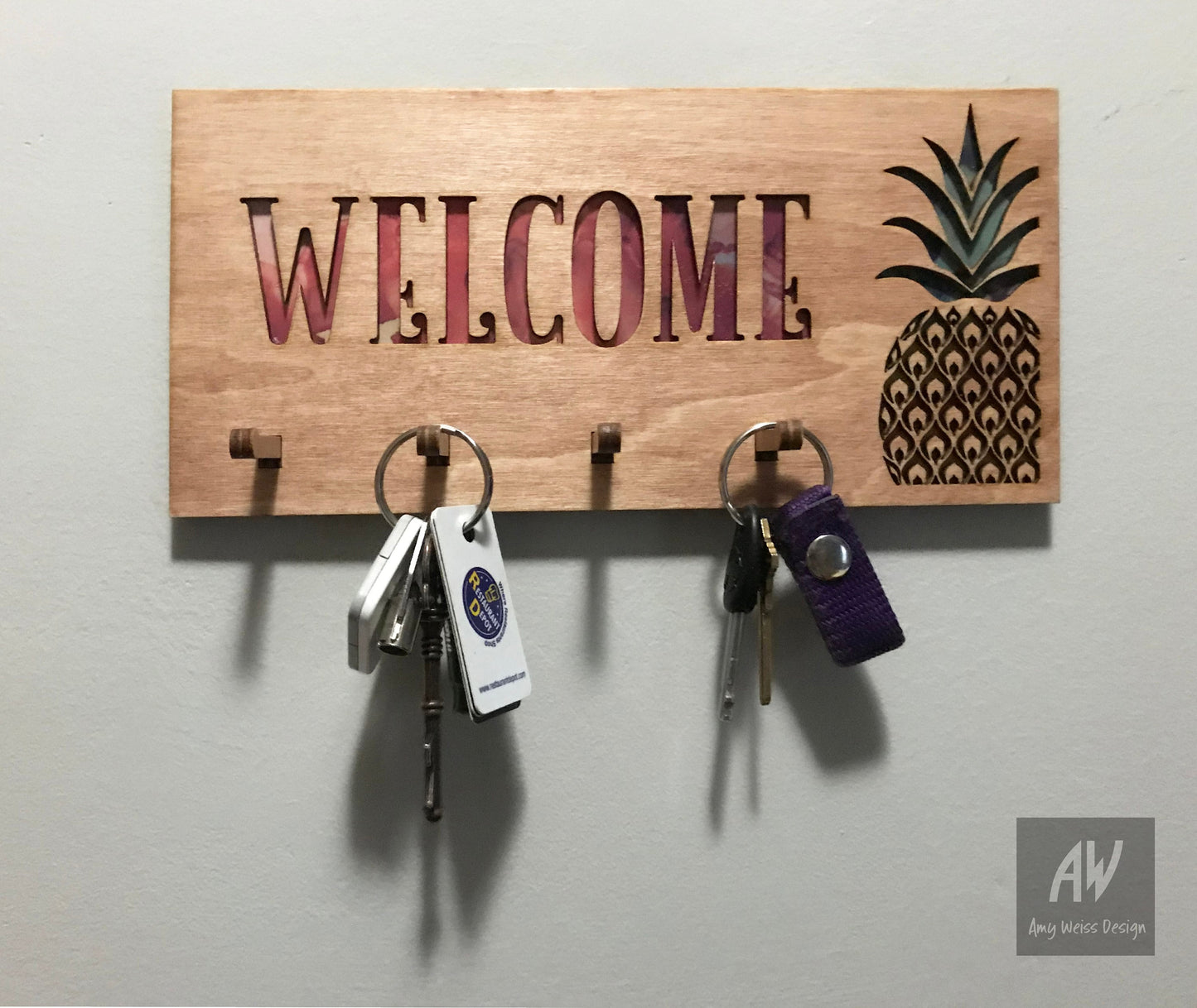 Key holder with the word "Welcome" and pineapple cutout. Red, yellow, and green showing through the holes. 4 pegs with keys on them.