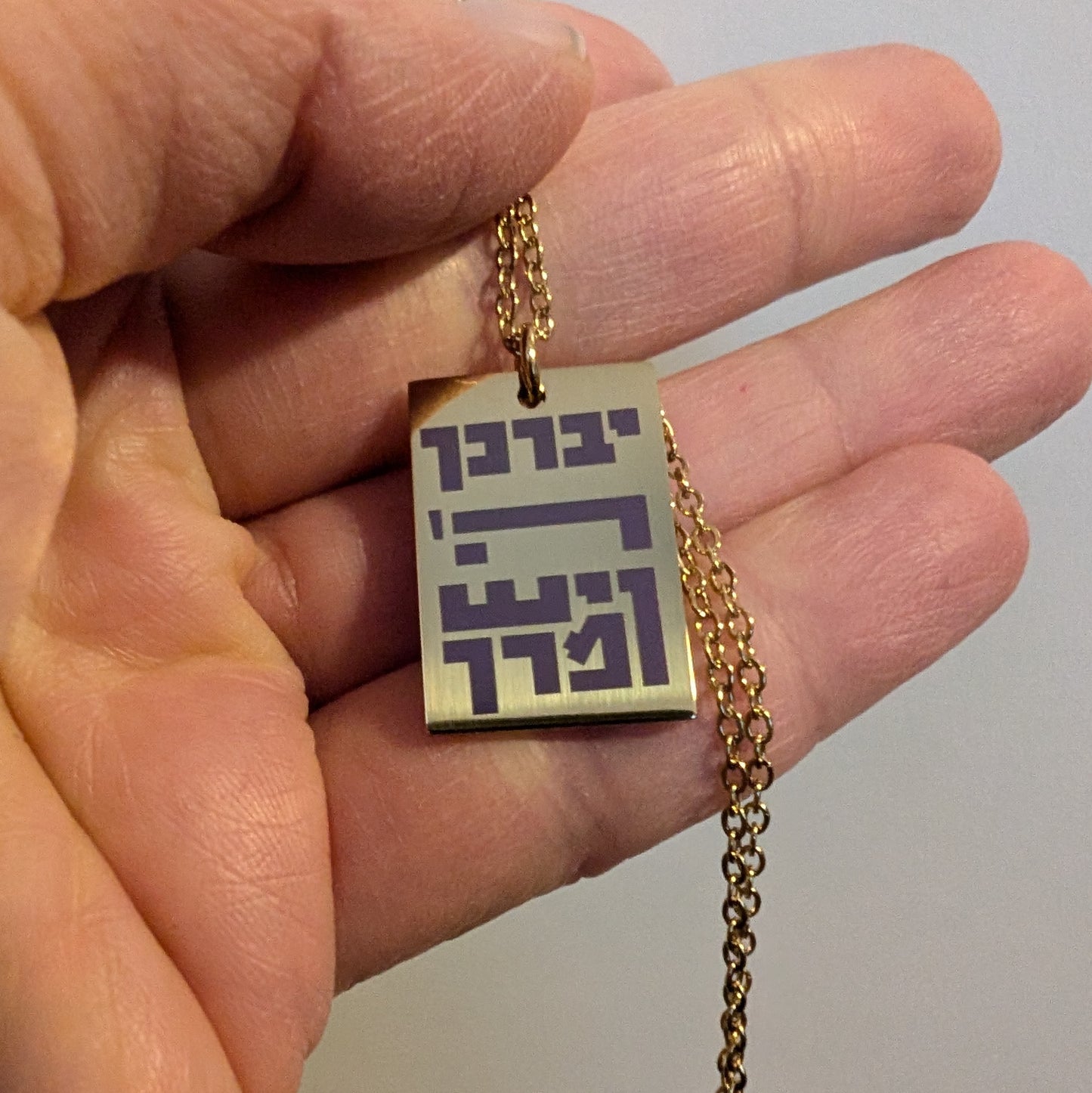 Gold colored rectangle pendant with rose colored hebrew letters spelling out the children's blessing.
יברך ה' וישמרך
"Yivarechecha Hashem ViYishmarecha"