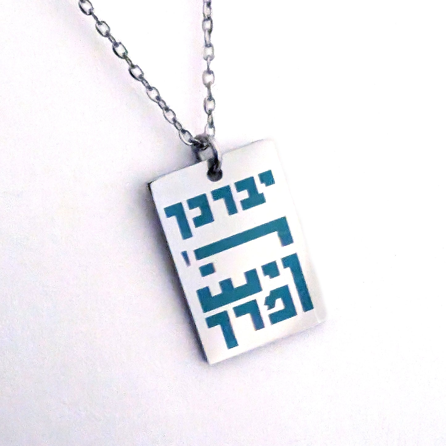 silver colored rectangle pendant with blue hebrew letters spelling out the children's blessing.
יברך ה' וישמרך
"Yivarechecha Hashem ViYishmarecha"