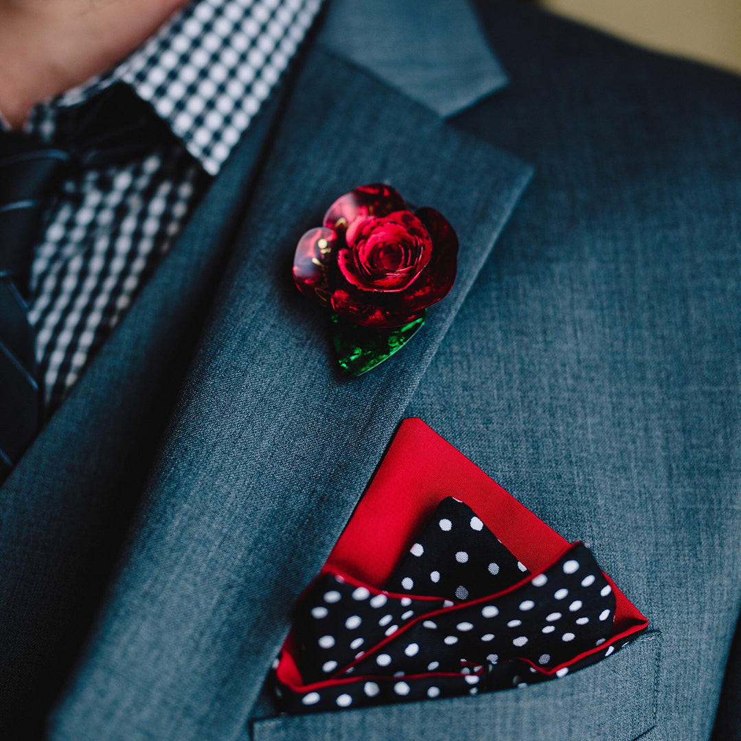 Red boutonniere made from guitar picks pinned onto lapel of suit jacket.