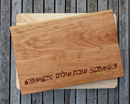 Maple color cutting board with pomegranates and the words shabbat shalom written in Hebrew characters.