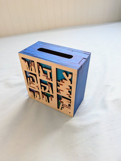 Small box with wooden front decorated with cutouts that look like bookshelves. Background color is shades of blue. View of the slot at the top to insert money.