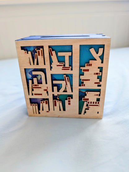 Small box with wooden front decorated with cutouts that look like bookshelves. Background color of bookshelves is shades of blue. 