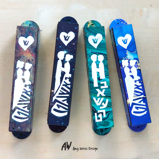4 mezuzah cases, two peole wearing dresses with an abstract colorful background and the word "Bashert" written in yiddish. The second mezuzah has a person wearing a suit and a person wearing a dress with a starry night sky background, the third is two people wearing suits with a green and black swirl pattern, and the fourth is two people wearing dresses with a blue painted background.