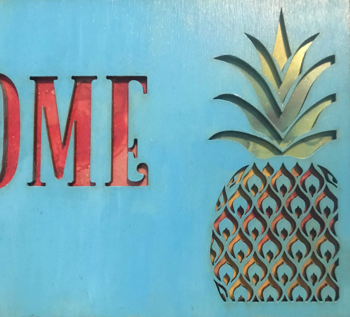 Close up of blue stained wood with red letters and orange, yellow, and green pineapple