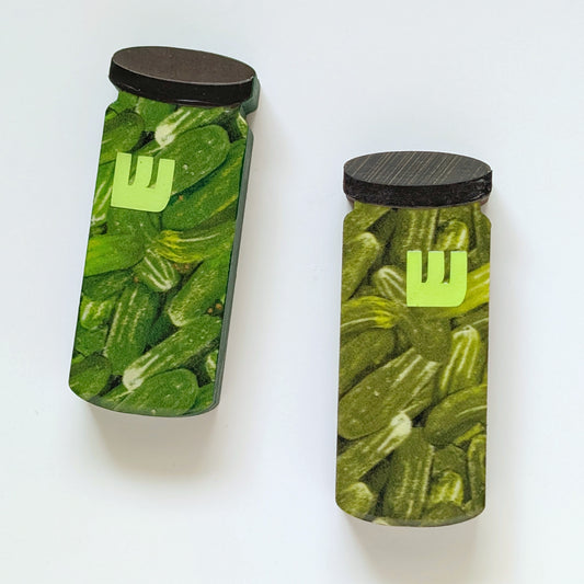Two mezuzah cases shaped like jars filled with pickles with black lids on a white background