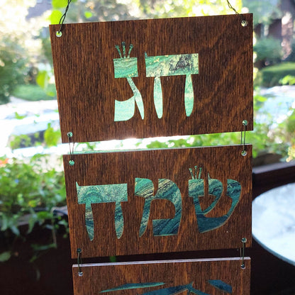 Top two panels of wooden sukkah decorations. Hebrew letters cut out with green and black pattern showing through.