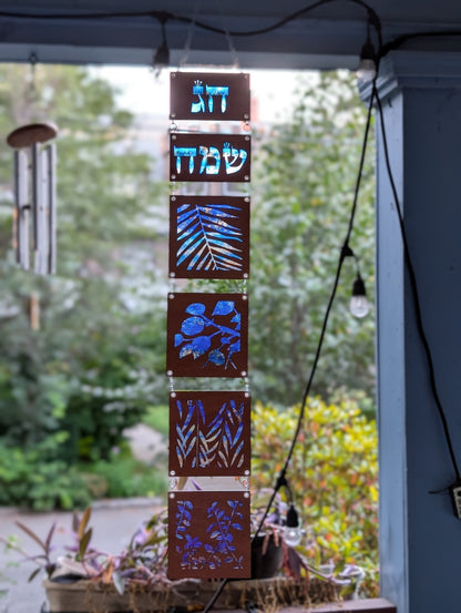 Decorative wood sukkah decoration with cut-out patterns of the elements of the lulav hanging outside.