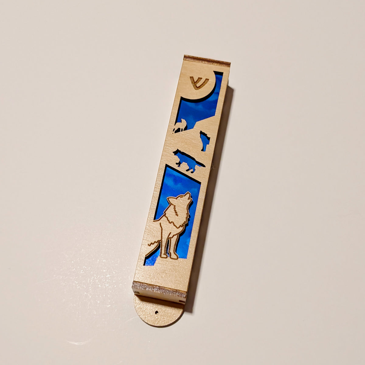 wooden mezuzah case on a white background. It is decorated with cutouts of wolves with blue from behind.